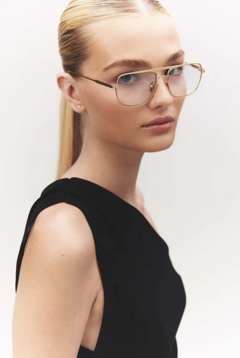 Woman wearing gold-framed glasses against a plain background