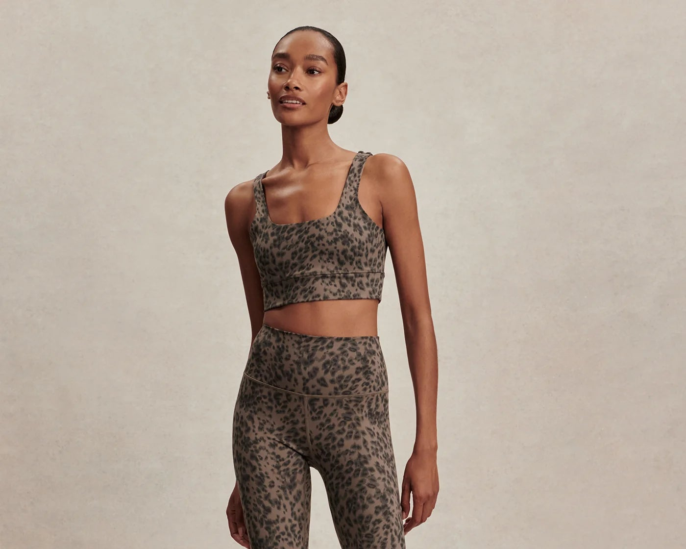 Woman wearing a leopard print sports bra and leggings on a beige background