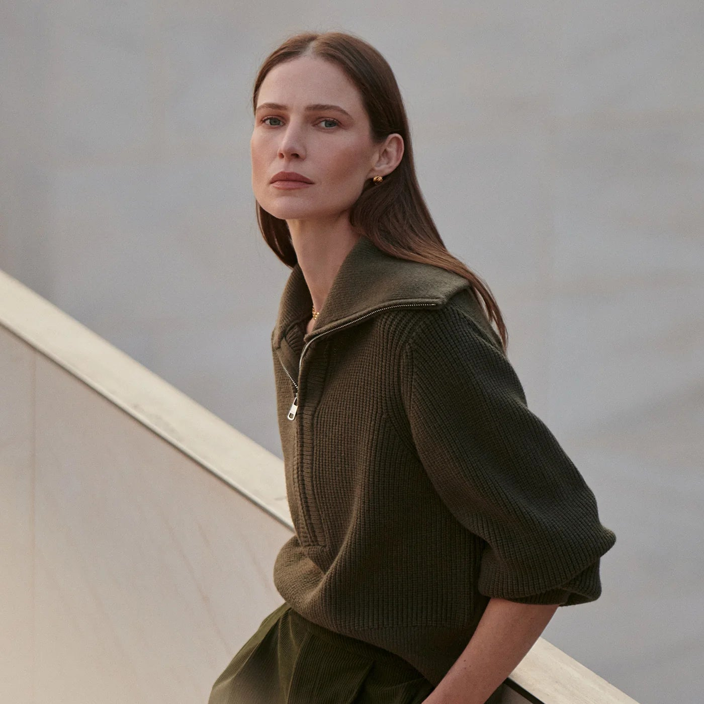 Woman wearing a green jacket standing on a staircase with a neutral background