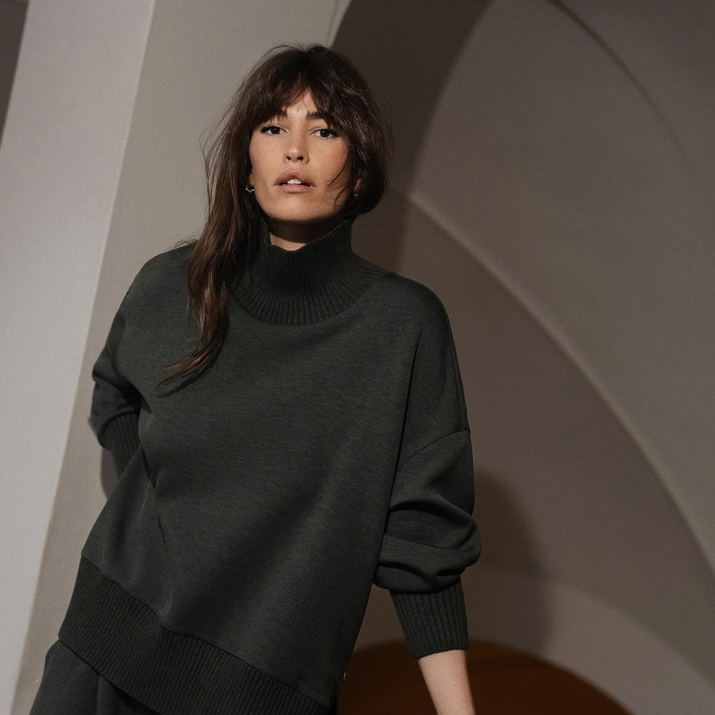 Woman wearing a dark green sweater against a neutral background